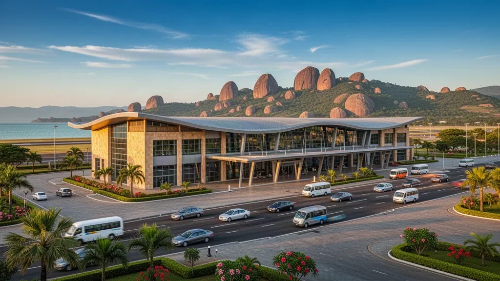 Modern glass terminal and drop-off lanes at Mwanza International Airport with granite hills and Lake Victoria under golden afternoon light