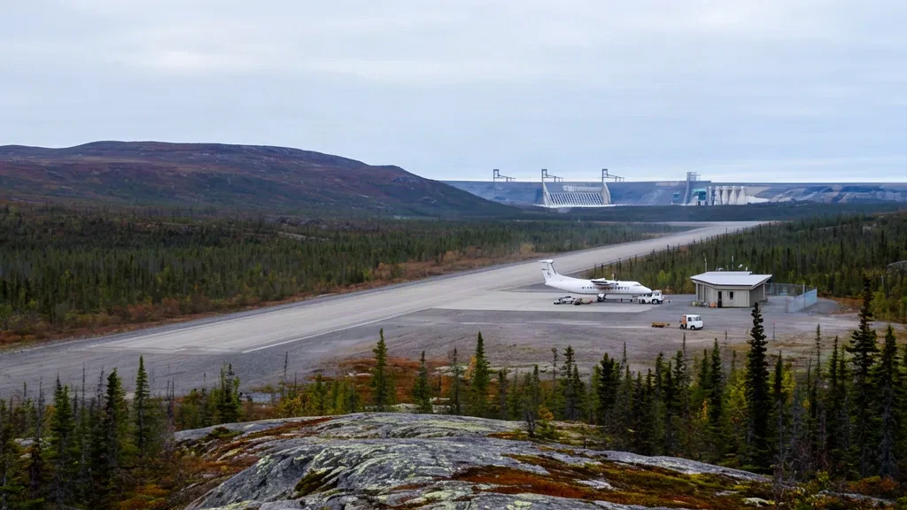 Pista di atterraggio in ghiaia remota e piccolo rifugio aeroportuale all'Aeroporto di La Grande-3 YAR nel Quebec settentrionale, circondati dalla foresta boreale sotto cieli coperti