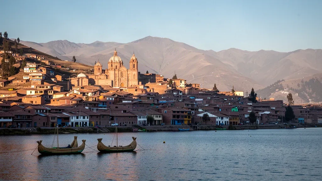 Stadt Puno am Hang über dem Titicacasee in der goldenen Stunde mit Schilfbooten und fernen Andenbergen