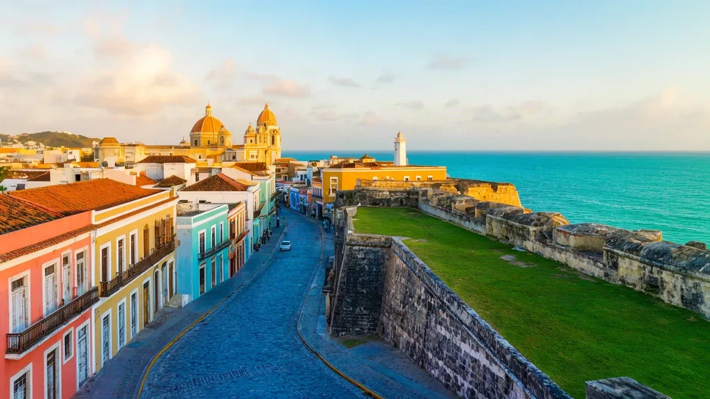 Vista durante la hora dorada sobre las coloridas calles coloniales del Viejo San Juan, los adoquines azules y la fortaleza de El Morro frente al océano Atlántico